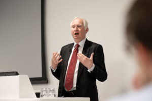 Daniel Zeichner stands in front of a screen addressing the room