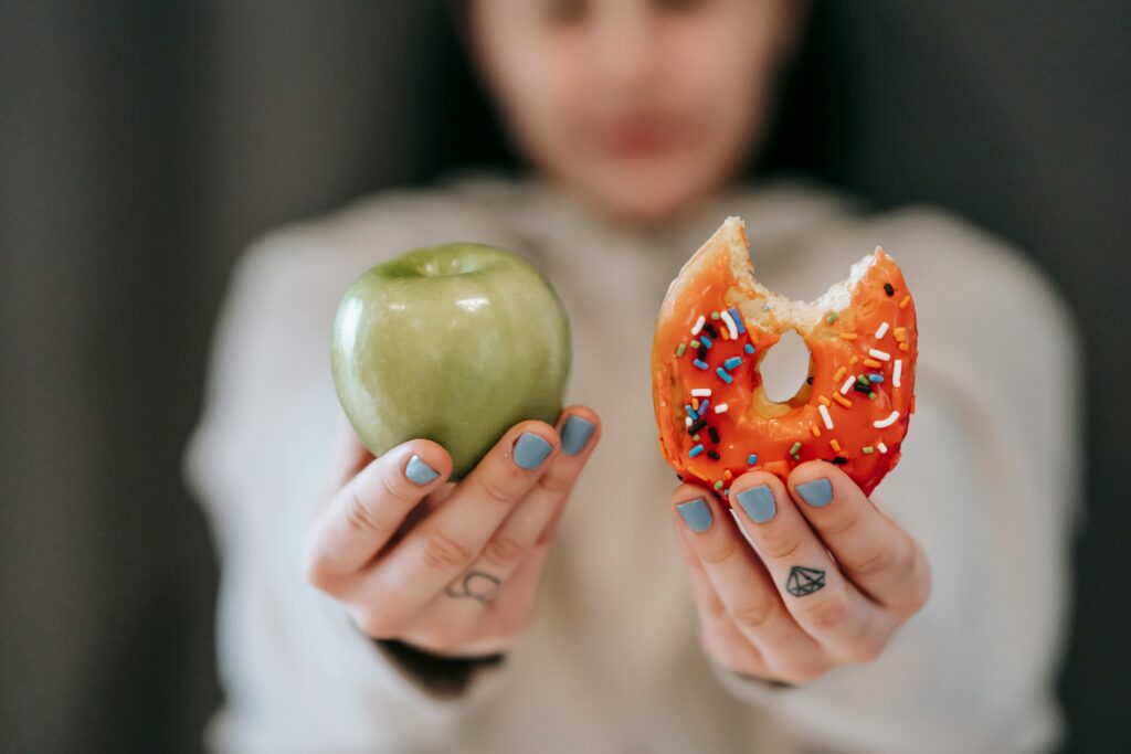Two hands, one holding a bright green apple, the other holding a doughnut.
