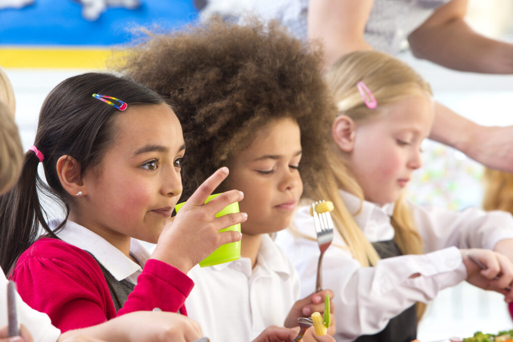 Three children, dressed in school uniform, sitting in a line eating their lunch